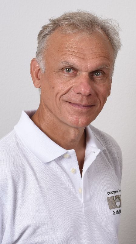 Portrait Dr. Nils Maier Ein Mann mittleren Alters mit grauem Haar, der ein weißes Polohemd trägt, schaut lächelnd in die Kamera.
